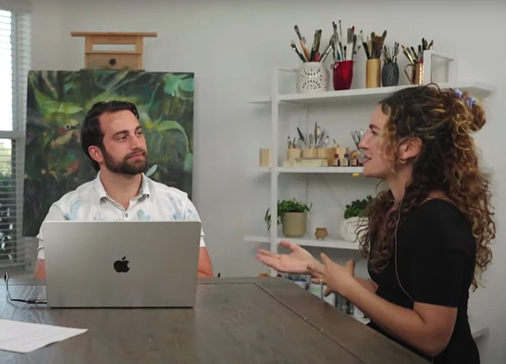 man and women sitting at table with laptop art in background